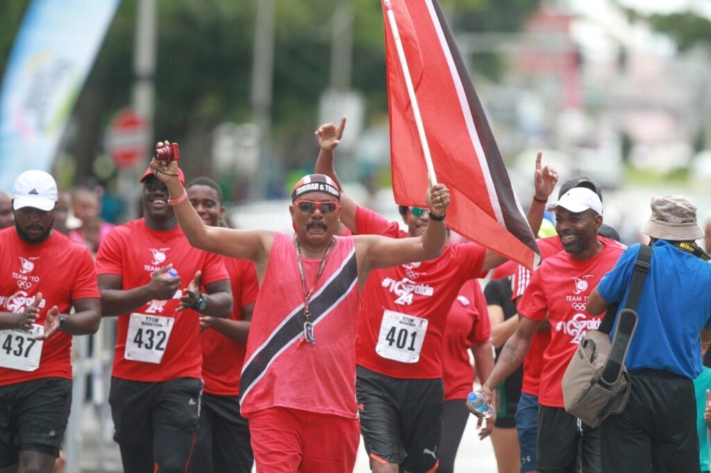 Joey "Flagman" Richardson, front, walks with Brian Lewis, TT Olympic Committee immediate past president and others seeking to raise funds for national athletes. - (Image obtained at newsday.co.tt)